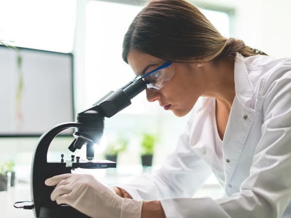 woman in lab coat looking through a microscope